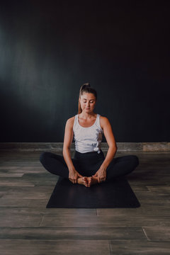 Diligent barefooted woman in sportswear performing bound angle pose exercise on mat in light contemporary gym