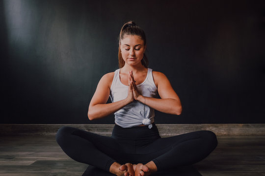 Calm relaxed female with eyes closed and namaste sitting in baddha konasana position on sports mat and concentrating while practicing yoga in dark modern studio