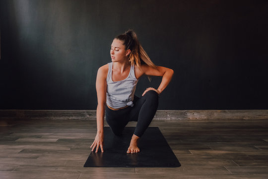 High angle of confident barefooted woman in sportswear stretching body in eka pada rajakapotasana two position on mat and looking away while training in spacious contemporary workout room