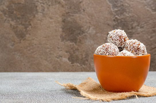 Energy balls of dates, peanuts, oats, sprinkled with coconut in a clay brown cup close-up on a dark background with copy space with place for text