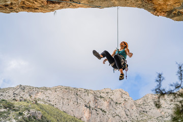 From below athletic female alpinist hanging on cliff under cloudy sky