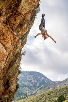 From below fearless young female alpinist enjoying climbing and adrenaline while hanging upside down from cliff
