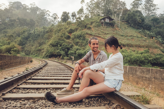 Side view of couple on vacation sitting on rails smiling and looking at each other near tropical green plants on hills in Sri Lanka Asia