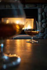 Low angle cognac drinks on table with fireplace burning in evening light. Depth of field.