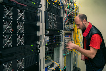 A technician connects fiber optic wires to a central router. A man works in a server room. An...