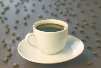 A Cup of coffee stands on a wooden table. Coffee beans scattered around