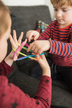 From above of little kids playing with colorful elastics on palms together at home 