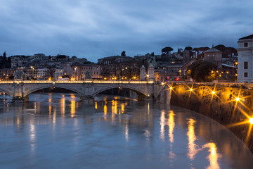 Tiber river bridge at night with light set and Rome view on background. Long exposure in Italy on cloudy day. Top view.