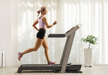 Fit woman running on a treadmill at home - obrazy, fototapety, plakaty
