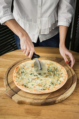 Cutting pizza with a pizza cutter, served on a wooden round board, natural light