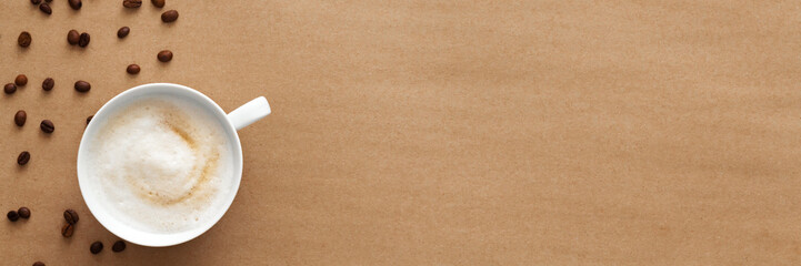 Cappuccino coffee on a brown empty background. View from above. Copy space with space for text. Foam on coffee, white cup, scattered coffee beans. Panorama