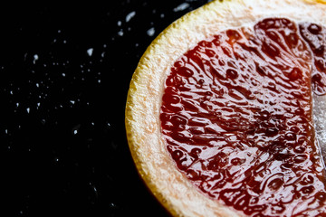grapefruit pulp with drops of moisture on a black mirror