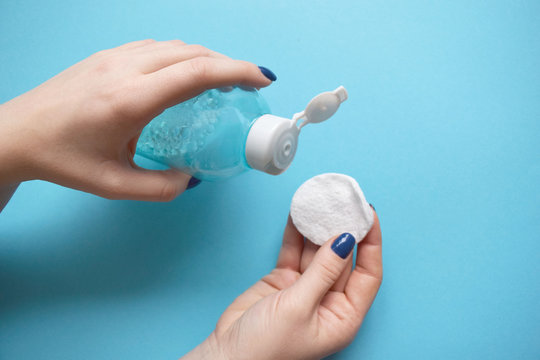 Woman's Hand Hold Cotton Pad And Tonic On A Blue Background. Beauty Concept, Clean Cosmetics.