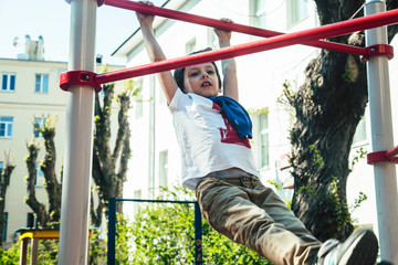 Fototapeta premium little cute blond boy hanging on playground outside, alone training with fun, lifestyle children concept