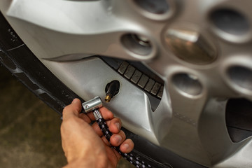  Topic of problems with the car. hand holding tip of car tire inflation pump. Tire inflation valve in the background. car repairs at home