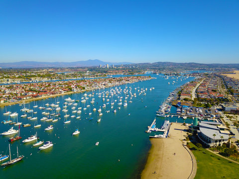 A Stunning Aerial Shot Of The Blue Ocean Water And White Boats And Yachts In The Harbor With A View Of The Cityscape Along The Beach With Blue Sky In Newport Beach California USA