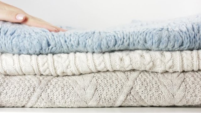 Cozy sweaters are lying in a pile. Woman hand touches them