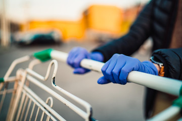 Close-up view of hands in rubber gloves pushing shopping carts.