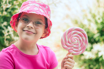 Little girl in a pink hat holding big lollipop