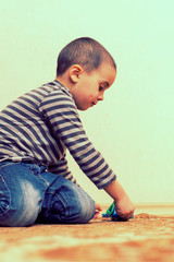 Naklejka premium Toddler boy is playing in the house on the floor. A kid boy playing toy blocks inside his house. Smiling child toddler plays animal toys at home or kindergarten. toned. vertical photo