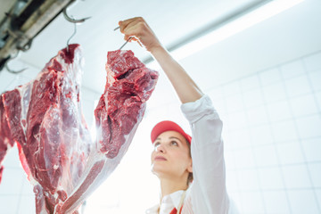 Butcher woman taking meat from hook to cut and sell it