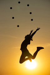 Silhouette of juggler jumping with balls on colorful sunset