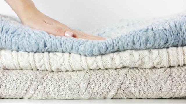 Cozy sweaters are lying in a pile. Woman hand touches them