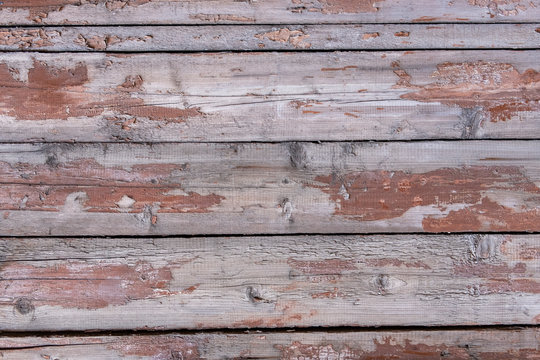 old wooden fence made of planks with peeling red paint with cracks and crevices. rough surface texture