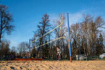 Fototapeta na wymiar A game of beach volleyball in cold weather in clothes. guy in front of volleyball net.