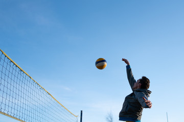 guy bounces a bouncing ball playing beach volleyball near the net. in cold weather in clothes. - Powered by Adobe