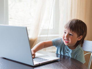 Curious toddler boy explores the laptop and presses buttons on computer keyboard.