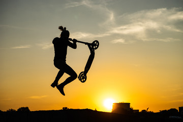 silhouette of a man riding and jumping on kick scooter with beautiful sunrise on background