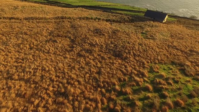 Cinematic aerial shot of a house in a wide field on the coastline of Ireland
