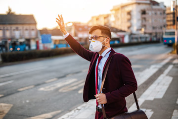 Young businessman with protective mask standing alone on empty street and waiting for bus or taxi. Virus pandemic or pollution concept.