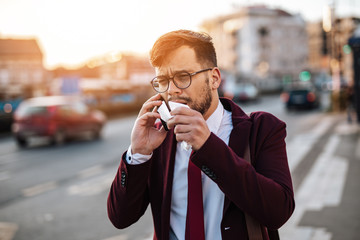 Young businessman with protective mask standing alone on empty street and waiting for bus or taxi. Virus pandemic or pollution concept.
