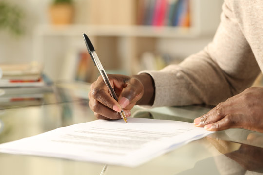 Black man hands signing document on a desk at home