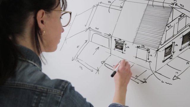 Close-up of a young female architect drawing a sketch for a new famaly home project. Concept of work on technical drawings