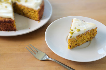 Piece of a small carrot cake with frosting and pistachios on a wooden table, traditional Easter pastry