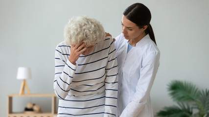 Supportive young woman doctor hold help sick senior old lady having dizziness or blurred vision, female nurse or caregiver assist support mature patient feeling unwell unhealthy, elderly care concept - obrazy, fototapety, plakaty