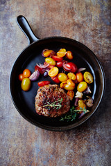 Fried hamburger steak with various cherry tomatoes and fresh herbs. Rustic background. Top view.