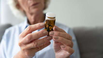Close up of mature old lady hold pills bottle thinking about taking it, sick pensive old woman read prescription consider having medicine, daily dose of prescribed drugs, elderly healthcare concept