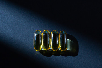 Omega-3 vitamins, fatty acids. Fish oil in yellow capsules on a black background.