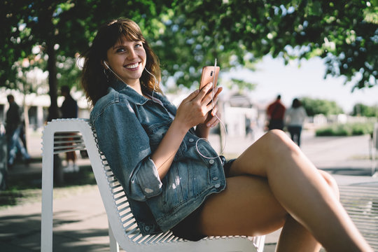 Happy millennial woman using smartphone while lounging on street in city