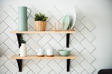 Kitchen utensils and tableware on wooden shelves. White tile on background. Kitchen details