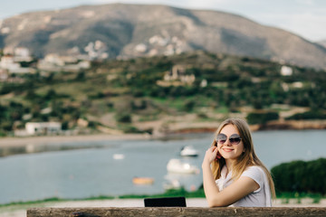 Happy young girl in glasses sits on a bench on a hill by the sea