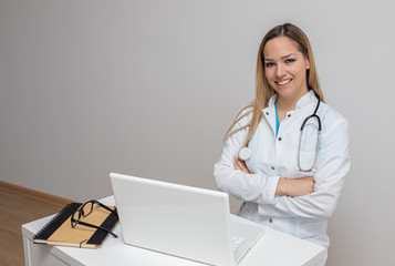 Confident doctor sitting arms crossed. Confident young woman doctor. Intern Doctor Young pretty woman in white clothes with a stethoscope posing and smiling.