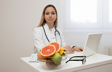 Obraz na płótnie Canvas Female nutritionist with fruits working at her desk. Smiling nutritionist in her office, she is showing healthy vegetables and fruits, healthcare and diet concept. 