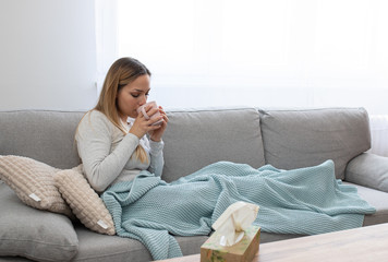 Sick woman sitting under the blanket. Sick woman with seasonal infections, flu, allergy lying in bed. Sick woman covered with a blanket lying in bed with high fever and a flu, resting and drinking tea