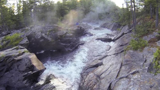 Smooth drone shot following the creek downstream revealing a young man trough the fog during sunrise