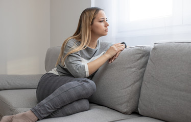 Obraz premium Sad and depressed woman sitting on sofa and looking at distance. Woman bored at home.